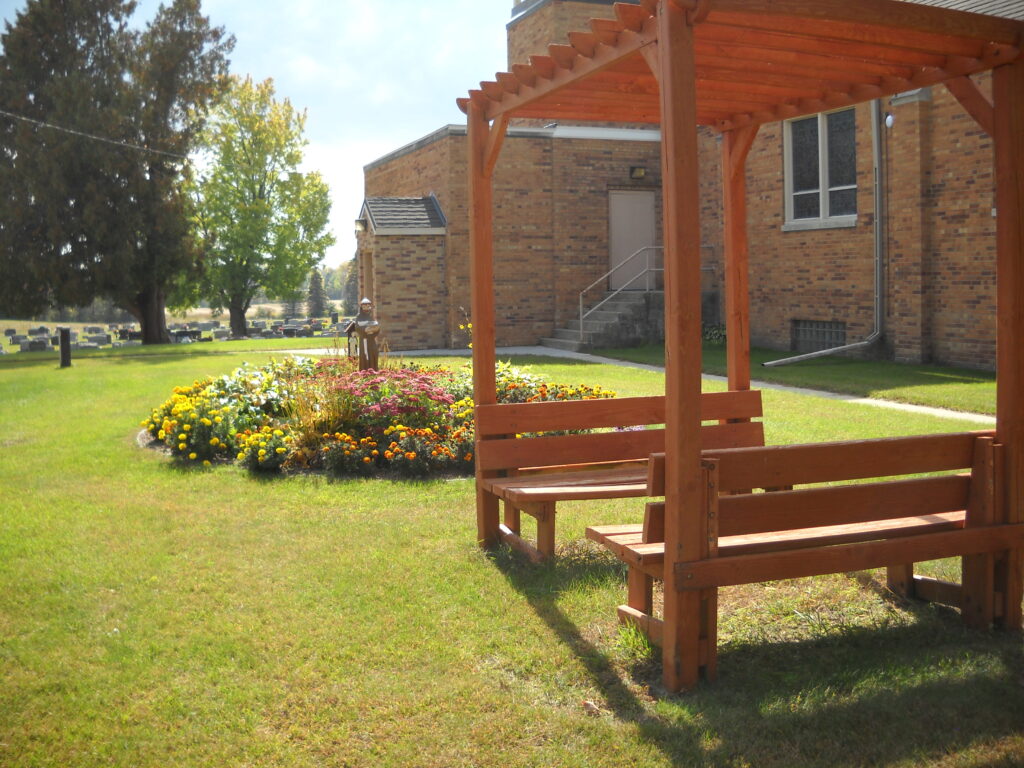 a bench with an overhang sitting next to a flower garden in summer - widows club